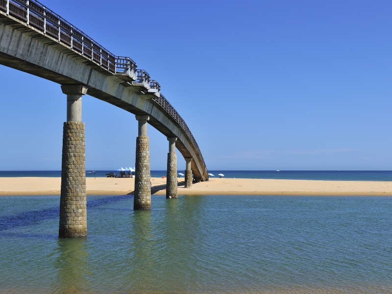 A pedestrian bridge leading out to a thin strip of sandy beach called Fulong