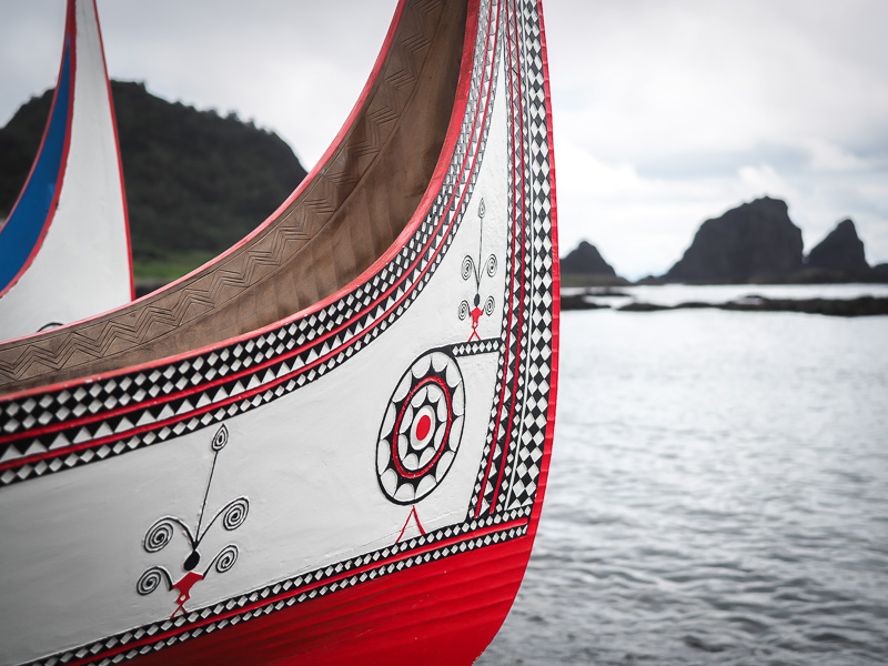 Close up of white and red canoes made by the Tao tribe on Orchid Island with water and small rocky islands in background