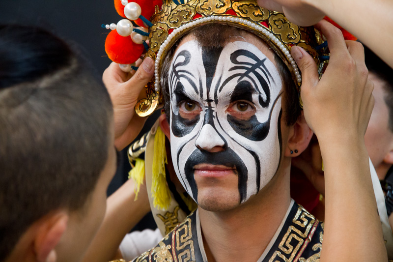 A Taiwanese man placing a Taiwanese opera crown on Nick Kembel's head with his face painted black and white