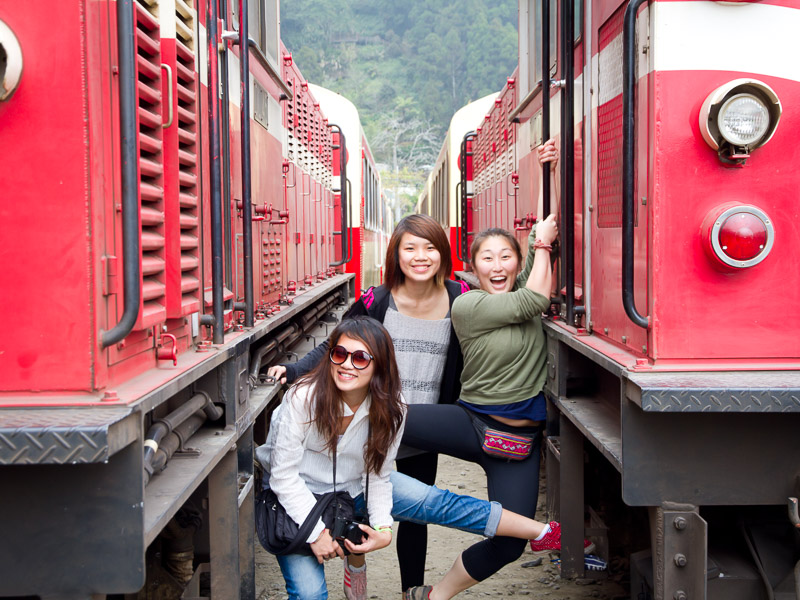 Three women standing between two red train cars at Fenqihu station