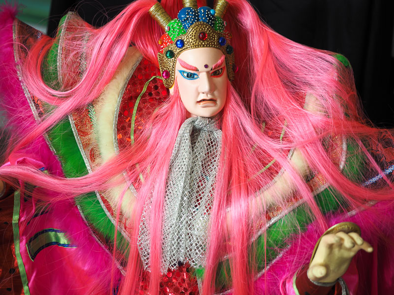 Close up of a traditional Taiwanese hand puppet with bright pink hair and green and green costume