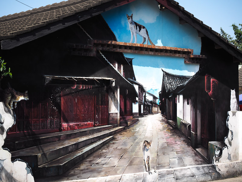A mural covering a whole side of a traditional Taiwanese house, showing some cats walking down a traditional lane