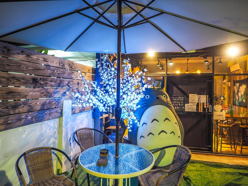 A Totoro statue and lights under an umbrella, in the outdoor seating area at a hostel in Lukang