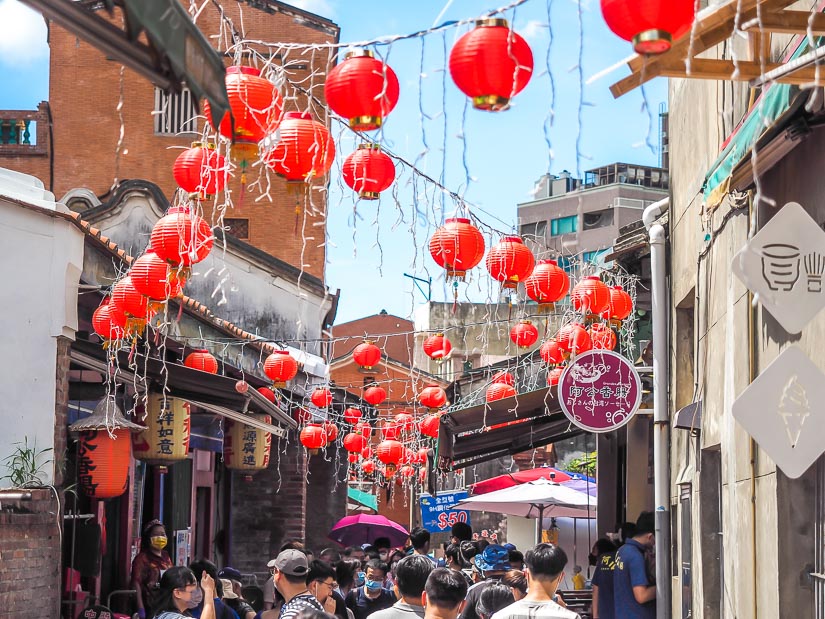 Red lanterns hanging above a crowd of people walking through a narrow old street in Lukang, Changhua