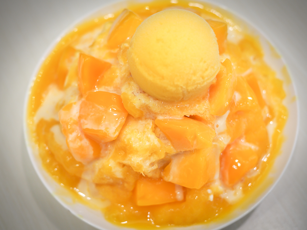 A heaping bowl of mango shaved ice, with chunks of mango and mango ice cream