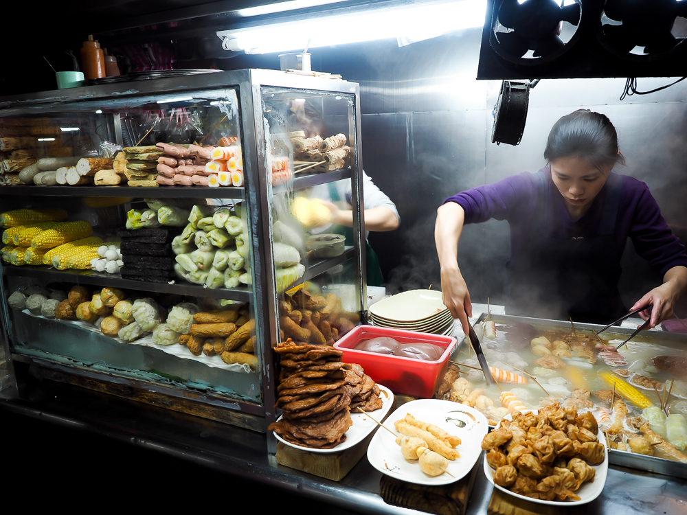 A woman food vendor scooping some food in a steaming stall in Nanjichang Night Market