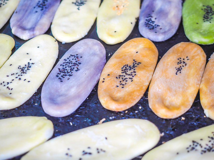 A grill with some colorful, flat, ox-tongue shaped cookies with black sesame seeds on top of them