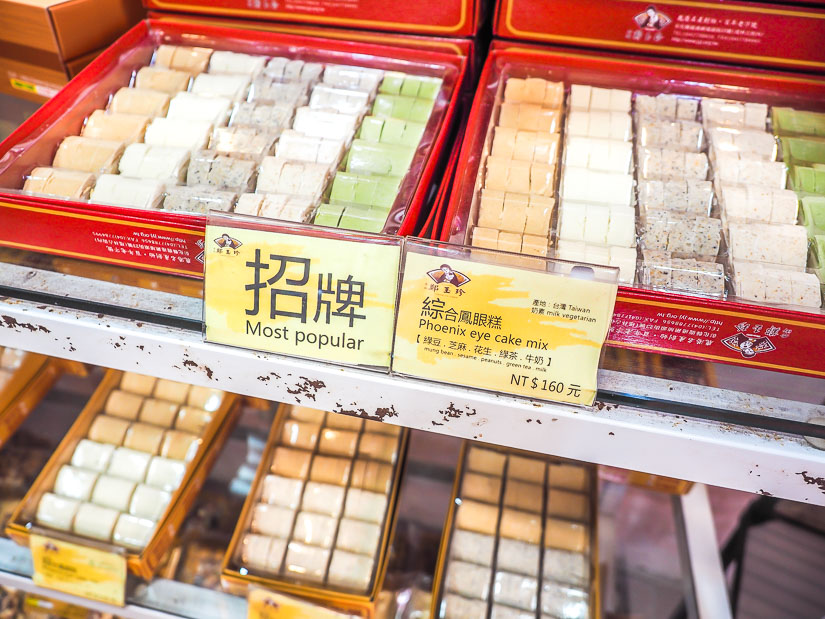 Several boxes of colorful phoenix eye cakes on a shelf in a store in Lukang, with yellow signs explaining what they are