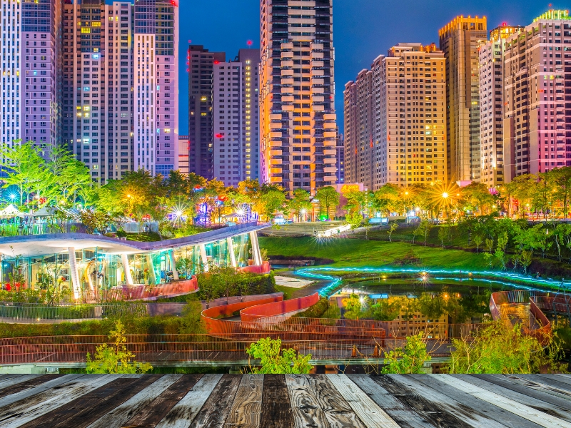 A park in Taichung city lit up at night with boardwalk in foreground and buildings in background