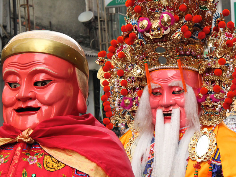 Two people wearing large costumes of gods walking down a street in Taipei