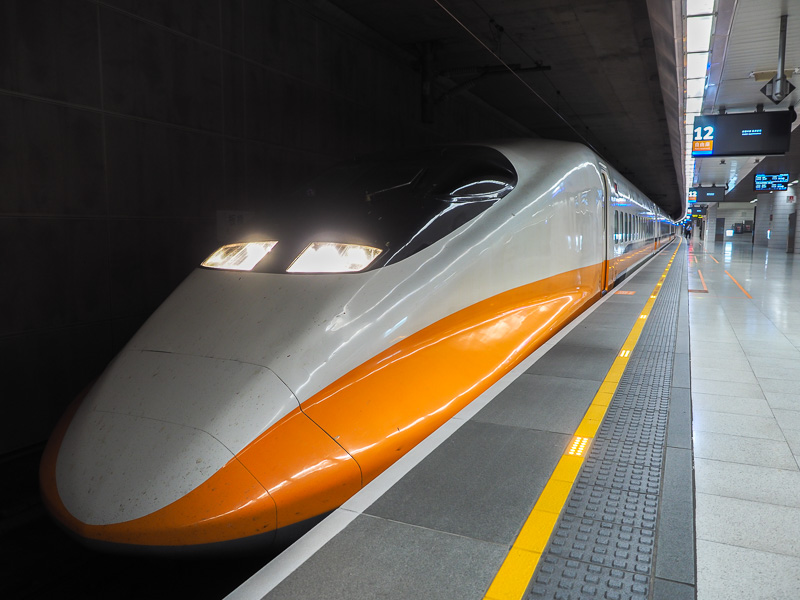 An orange and white bullet train parked in an underground station beside the platform