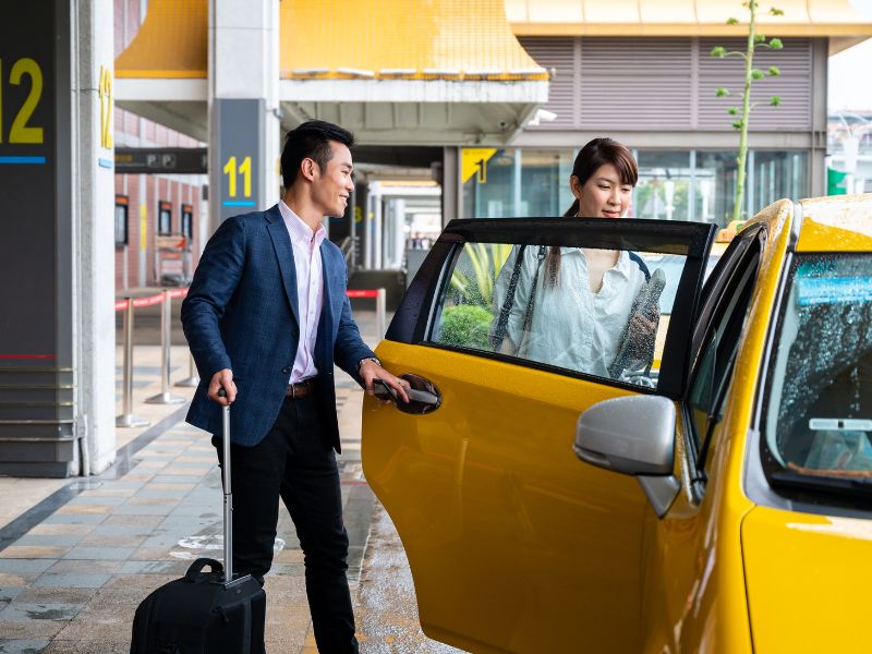 A man and woman getting into a yellow taxi at the airport.