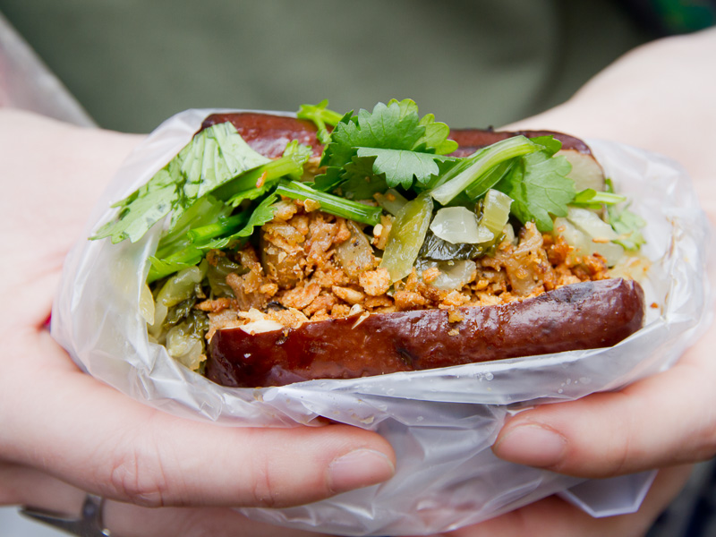 Close up of two hands holding a big chunk of tofu stuffed with cilantro, pickled vegetables, and other ingredients, in a plastic bag