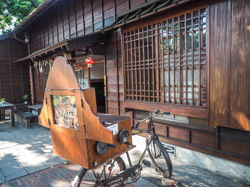 An old bicycle cart with storyboard attached to it in front of a Japanese style wooden building