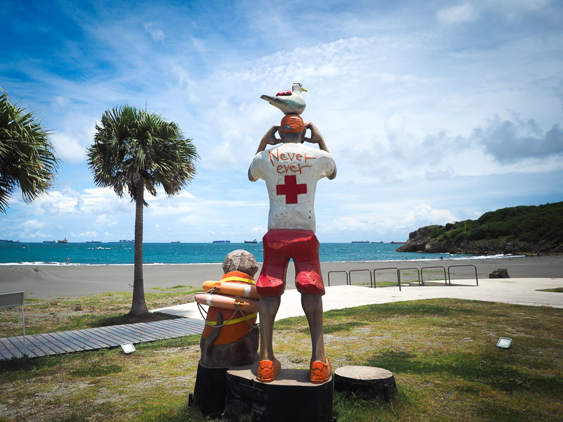 A statue of a lifeguard and dog facing a beach on Cijin Island in Kaohsiung
