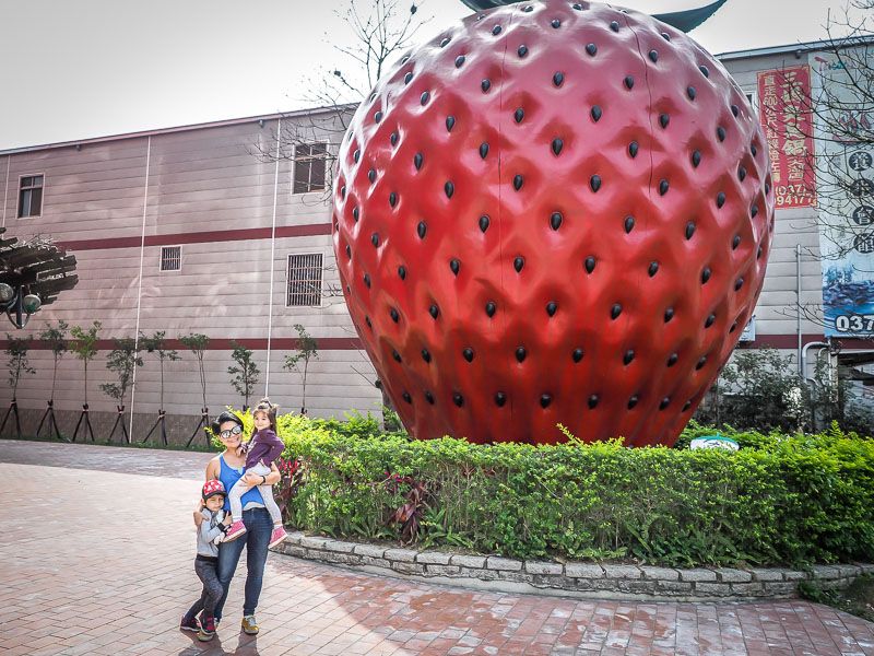 A Taiwanese woman and her two kids posing in front of a giant strawberry statue