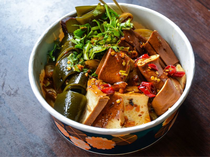 A paper bowl containing chunks of tofu, kep, cilantro, chilies, and sauce on Daxi Old Street