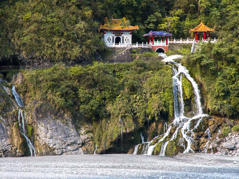 A large Taiwanese shrine with waterfall pouring out from it down to a river below