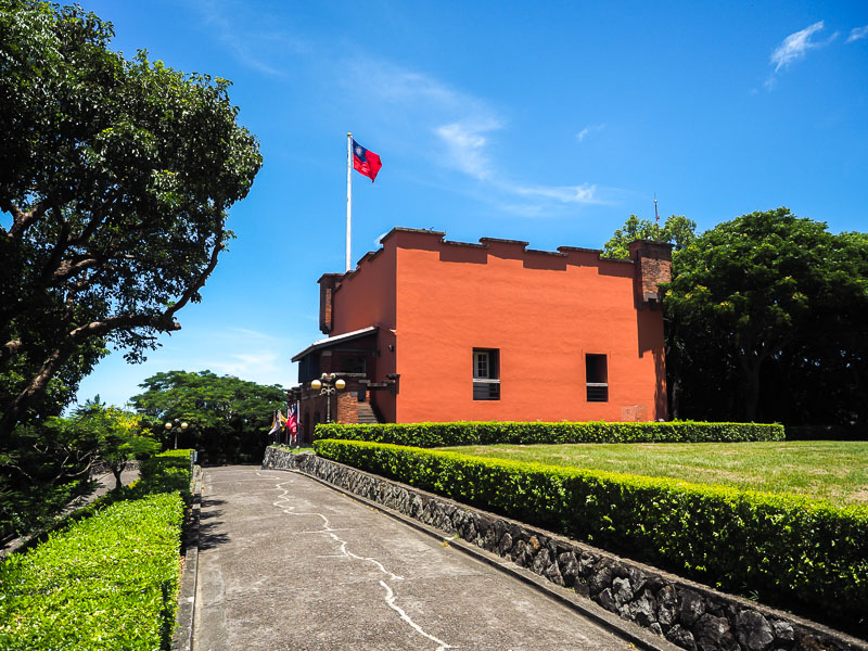 A bright red fort with Taiwan flag flying above and path leading to it in Tamsui