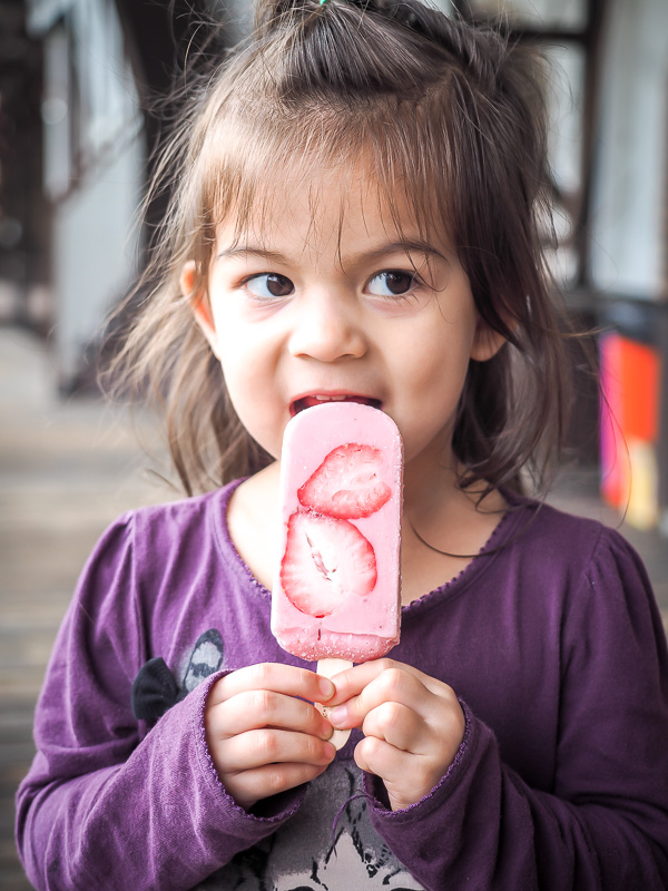 A young girl biking a pink popsicle that has slices of real strawberry in it