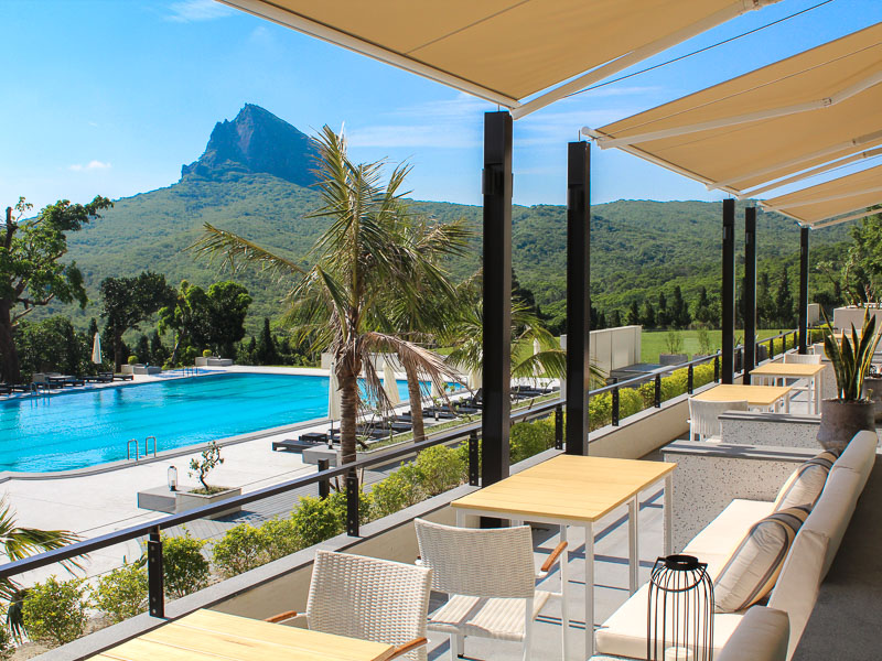 Chairs on a balcony overlooking a hotel swimming pool with a mountain in the distance