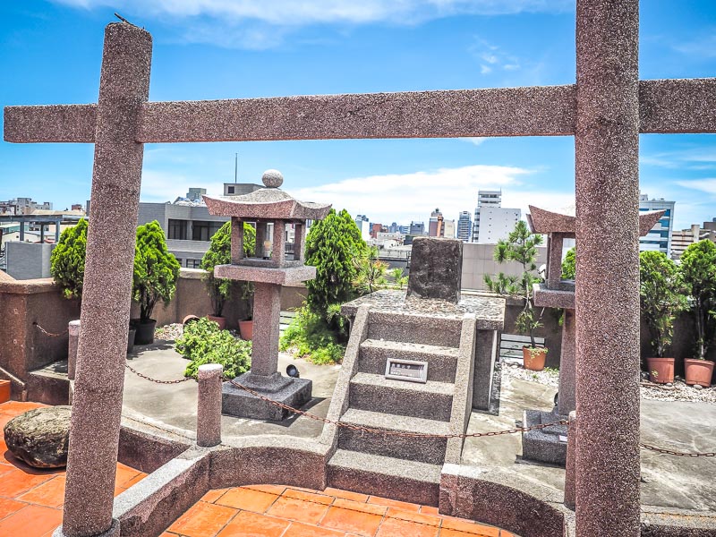 A stone Japanese gate and shrine on the roof of a building overlooking Tainan