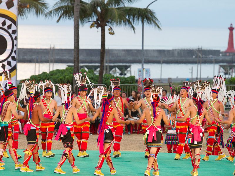 Some Taiwanese aboriginals doing a dance performance on a stage in Hualien with a harbor and palm trees in the background