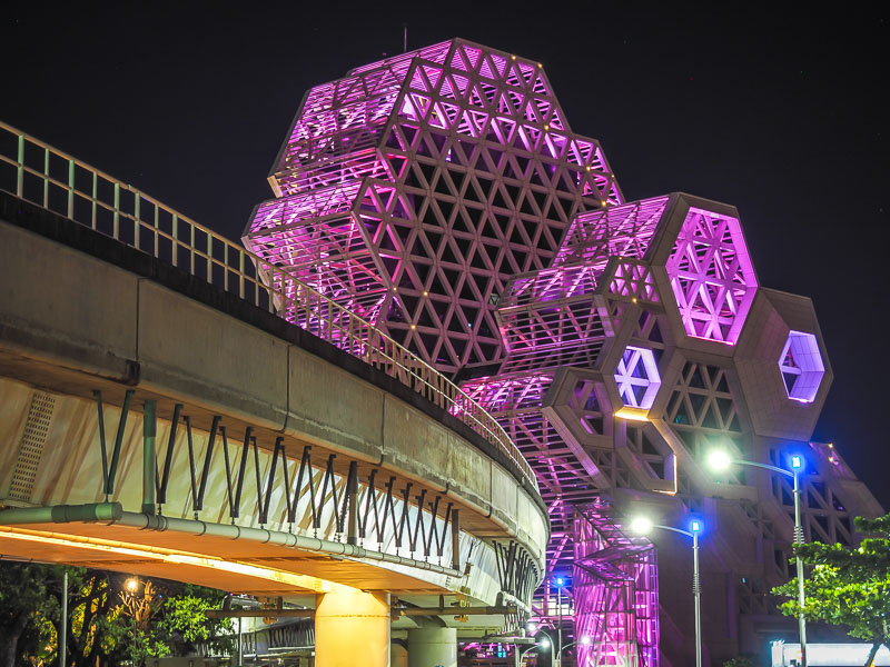 A huge modern building with geometric design lit up with purple lights at night