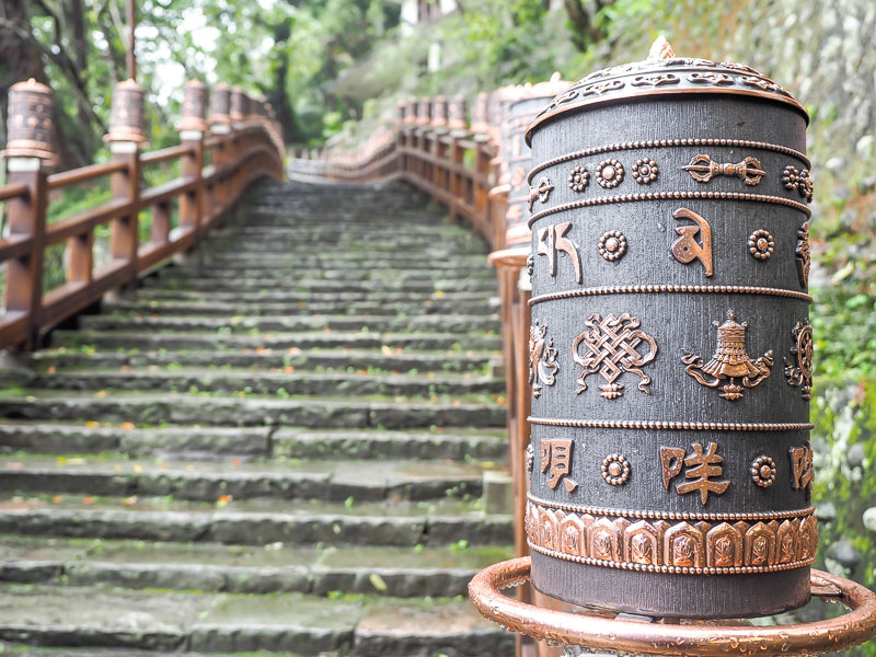 A prayer wheel with staircase of a hiking trail going up behind it