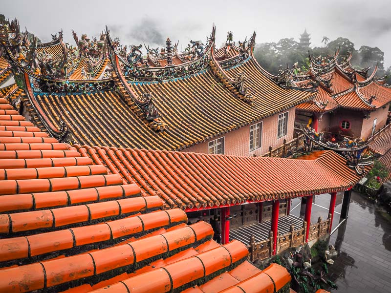 Looking down at the orange roof tiles of a temple with misty mountaintops in the background