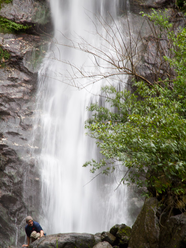 A man climbing on rocks at the bottom of a tall waterfall