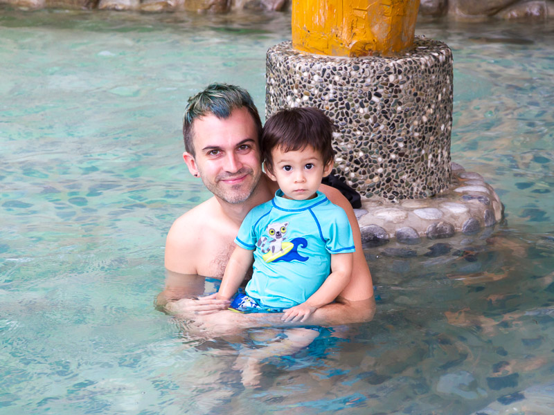 Nick Kembel with blue hair holding his young son in a hot spring in Jianshi, Hsinchu