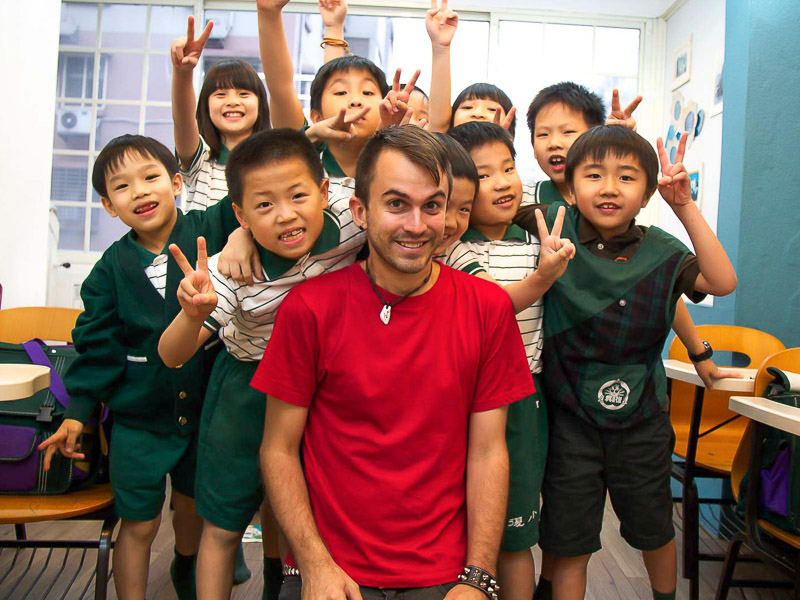 Nick Kembel in a red shirt surrounded buy a group of Taiwanese students wearings school uniforms and posing happily for the camera