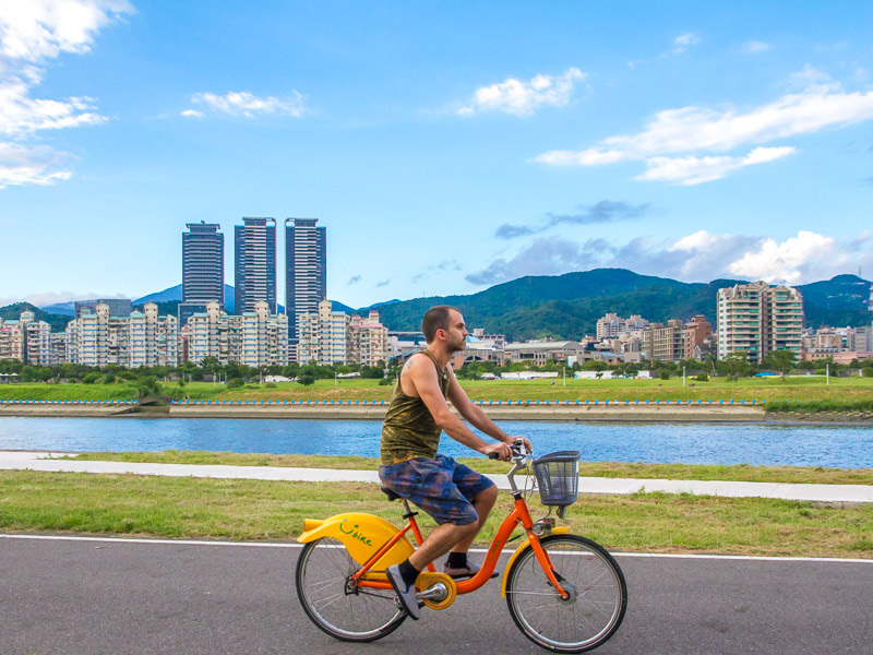 Nick Kembel riding on a yellow and orange YouBike in Taipei riverside park