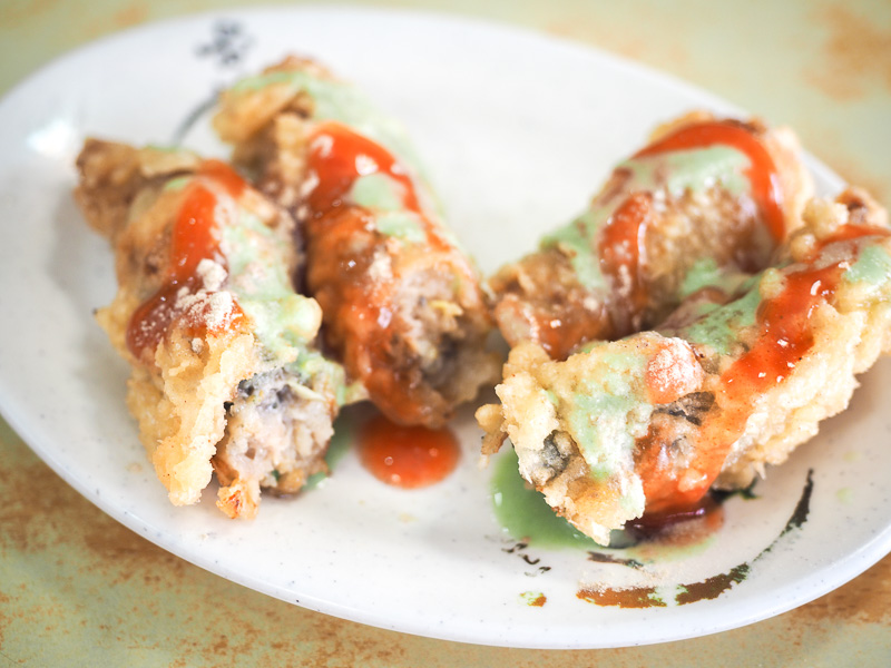 A white plate with four pieces of deep fried oyster rolls with spicy red and green sauce on them