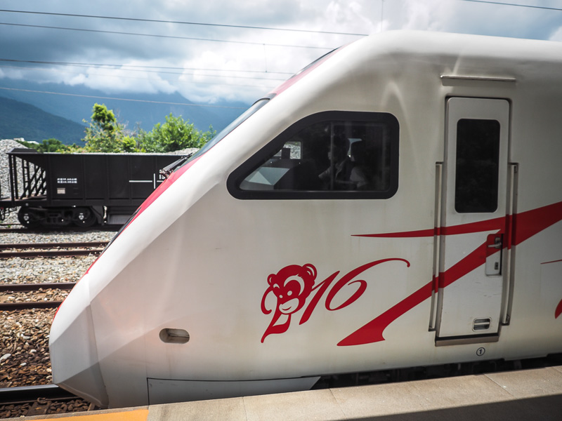 The front white car of a train with red designs in red, parked at a train station platform outdoors