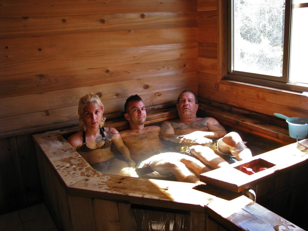 Nick Kembel, his sister, and his father inside a wooden hot spring tub