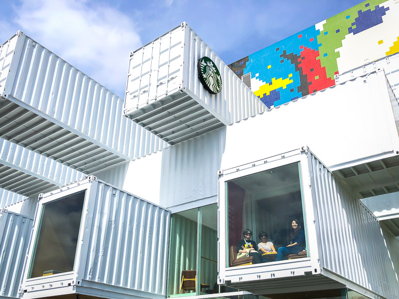 A Starbucks cafe made out of shipping containers piled on top of each other, with some people visiting having coffee inside one of them