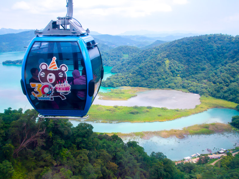 A blue cable car with cute bear on the side and Sun Moon Lake far below