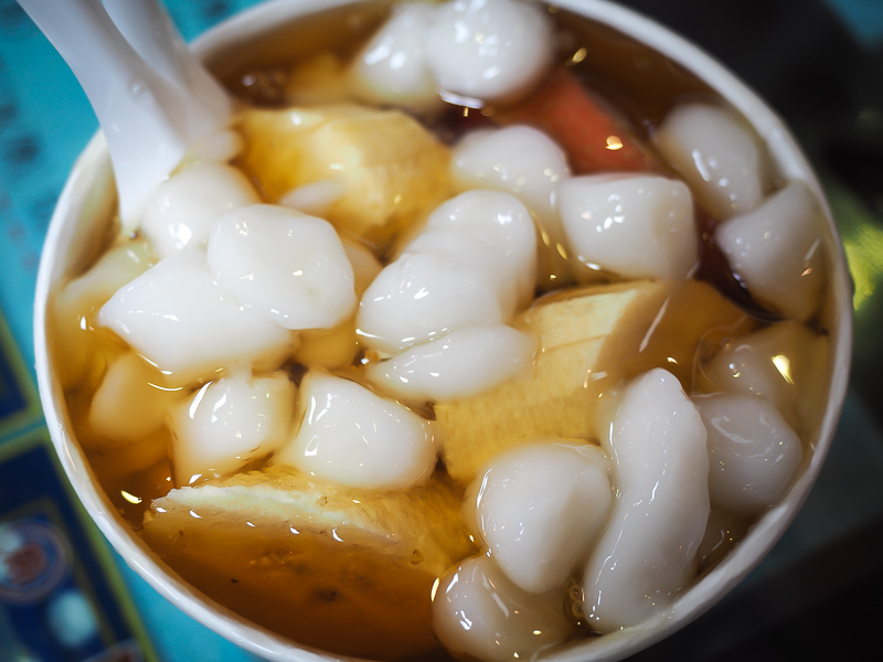 close up of a bowl of shaved ice with fruits, honey, and rice balls on top