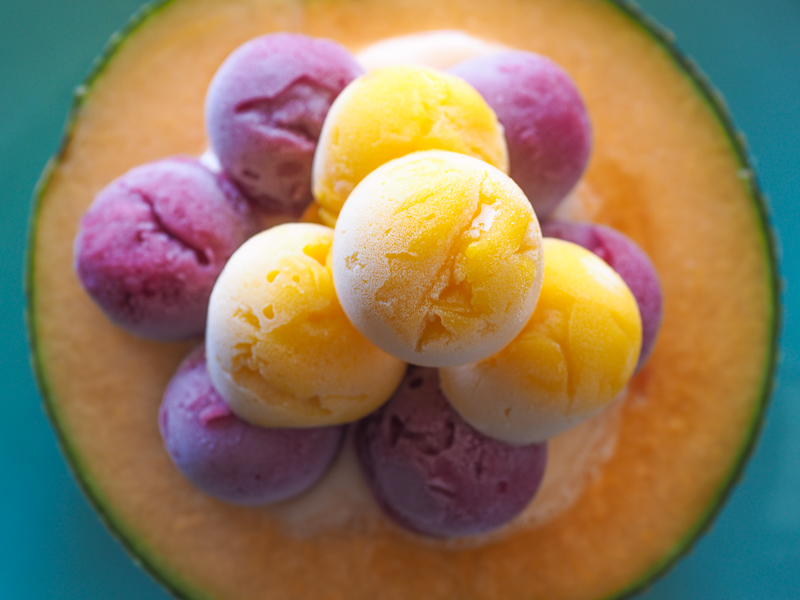 An orange cantaloupe cut in half and filled with scoops of orange and purple ice cream