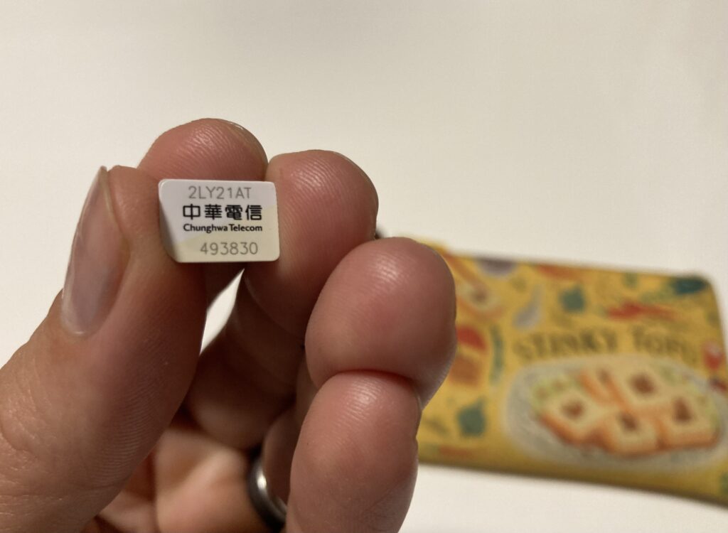 A hand holding up a tiny Taiwan Chunghwa SIM card with a yellow wallet in the background
