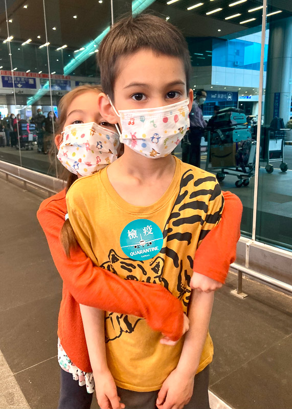 Two kids wearing masks and with a sticker on their shirt that says Quarantine