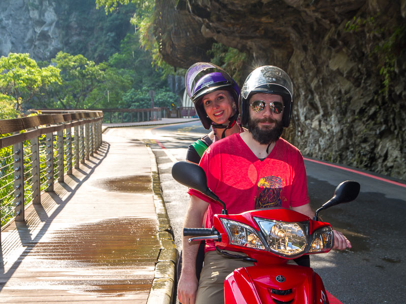 A couple sitting on a scooter wearing helmets on a road in Taroko Gorge