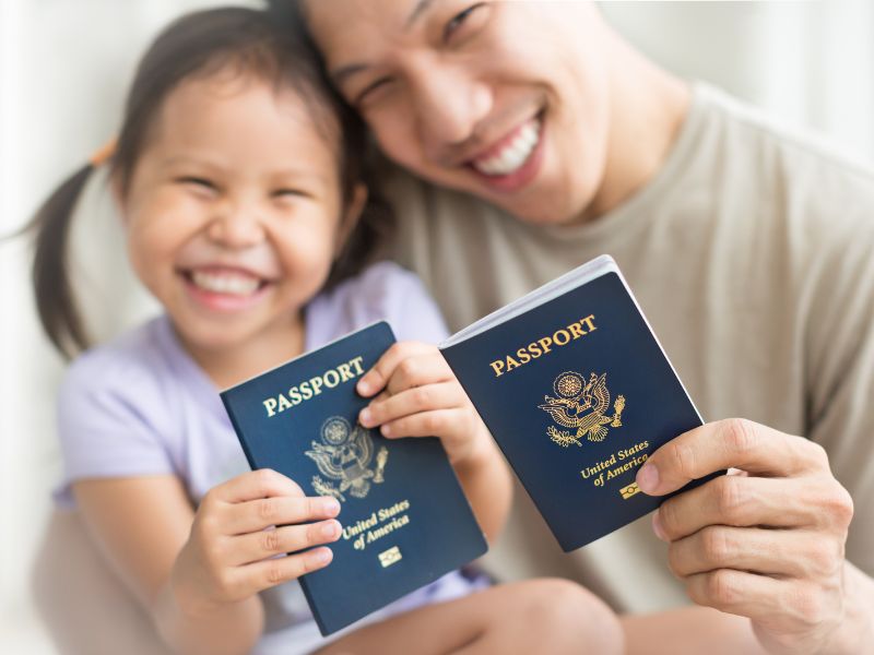 An Asian parent and child holding up their USA passports to the camera