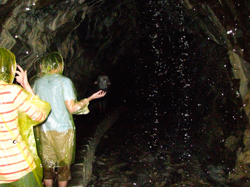 Some people wearing yellow rain coats walking through a dark cave with water falling down on them