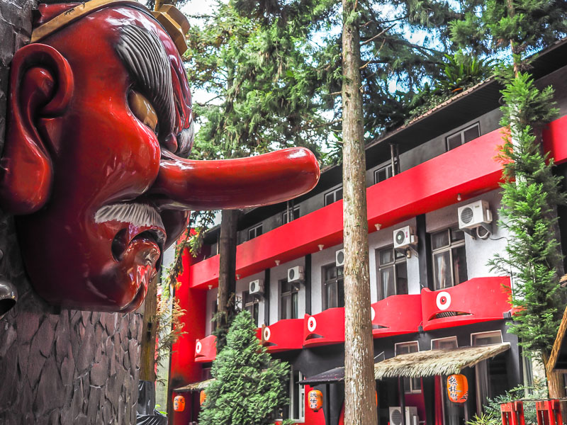 A giant red monster statue with long nose in the foreground and red balconies with monster faces on them in the background