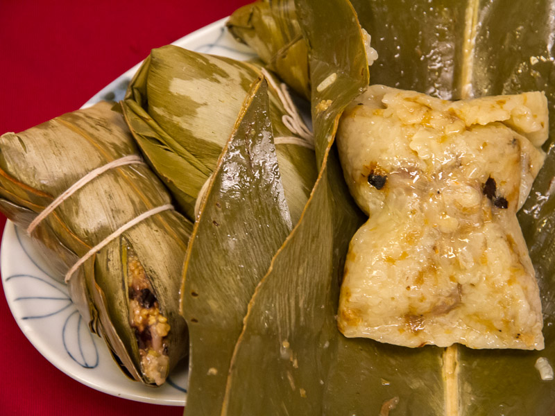 Some bundles of rice wrapped in large leaves and steamed, with one of them opened