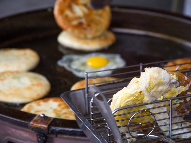 An egg frying on a grill with green onion cakes around it