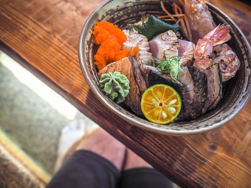 Looking down at a bowl of Japanese food on a table, and Nick Kembel's feet below soaking in hot water